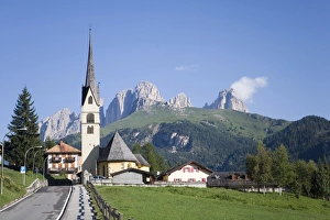 A church in the village of Alba with the rugged peaks of the Sassolungo in the distance A church in the village of Alba with the rugged peaks of the Sassolungo in the distance