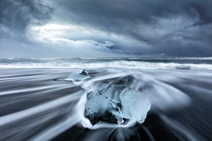 Glacier ice on black sand beach with waves washing up the beach on a stormy winter day Glacier ice on black sand beach with waves washing up the beach on a stormy winter day
