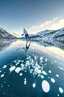 Ice hockey player skating on frozen Lake Sils covered of bubbles, Engadine Ice hockey player skating on frozen Lake Sils covered of bubbles, Engadine