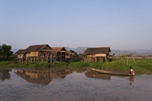 A man paddles his canoe past one of the floating villages on Inle Lake, Myanmar (Burma) A man paddles his canoe past one of the floating villages on Inle Lake, Myanmar (Burma)