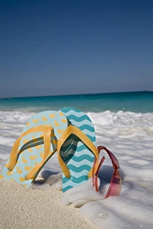 Two mismatched beach flip-flops with red sunglasses in the surf on a Caribbean beach Two mismatched beach flip-flops with red sunglasses in the surf on a Caribbean beach