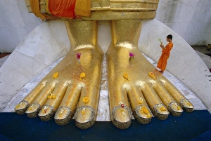 Novice monk praying at the feet of Giant Buddha statue Novice monk praying at the feet of Giant Buddha statue