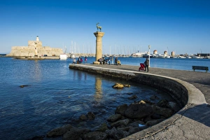 The old Agios Nikolaos fortress and lighthouse in Mandraki Harbour with deer statue in foreground The old Agios Nikolaos fortress and lighthouse in Mandraki Harbour with deer statue in foreground