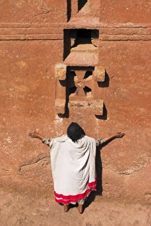 Pilgrim with arms outstretched praying under windows on monolithic church of Bet Maryam Pilgrim with arms outstretched praying under windows on monolithic church of Bet Maryam