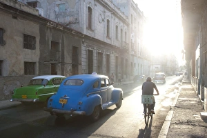 Street scene bathed in early morning sunlight showing old American cars and cyclists Street scene bathed in early morning sunlight showing old American cars and cyclists