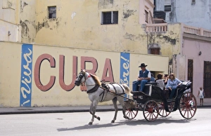 Tourists in a horse carriage passing a wall sign saying Live free Cuba Tourists in a horse carriage passing a wall sign saying Live free Cuba