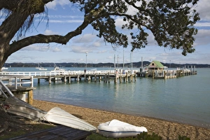 Upturned boats on beach with pier to wharf in bay framed by Pohutukawa tree branches Upturned boats on beach with pier to wharf in bay framed by Pohutukawa tree branches