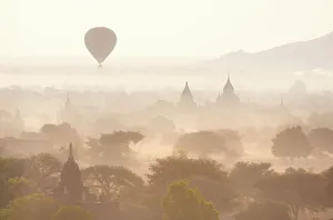 View over the temples of Bagan swathed in early morning mist, with hot air balloon drifting across the scene View over the temples of Bagan swathed in early morning mist, with hot air balloon drifting across the scene