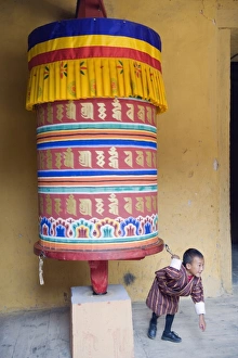 Prints of Young boy pulling a prayer wheel, Jakar Dzong, Castle of the White Bird, Jakar, Bumthang, Chokor Valley, Bhutan, Asia Related Prints: Bhutanese Landscape Print - Young Boy Pulling a Prayer Wheel
