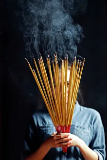 Young Chinese woman praying with big burning incense sticks in her hands Young Chinese woman praying with big burning incense sticks in her hands