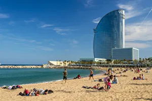 Barceloneta Beach in Barcelona, featuring golden sand, sunbathers, the Mediterranean Sea, and the distinctive sail-shaped W Hotel in the background.