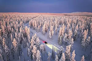 Finland Collection: Car traveling on icy road crossing the winter forest covered with snow from above, Lapland, Finland