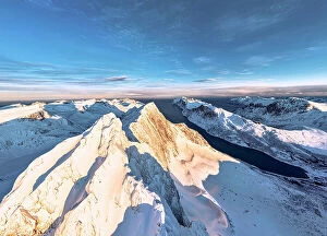 Q3 2023 Collection: Dramatic sky at dawn over majestic Breidtinden mountain peak covered with snow, aerial view