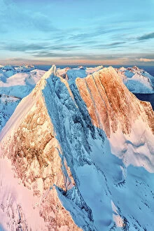 Norway Collection: Dramatic sunrise over the steep rocks of the snowy Breidtinden mountain peak, aerial view