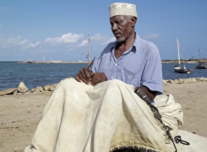 A fisherman repairs the sail of his wooden sailing boat A fisherman repairs the sail of his wooden sailing boat