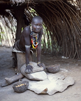 A Kwego woman grinds sorghum flour at the entrance to her hut A Kwego woman grinds sorghum flour at the entrance to her hut