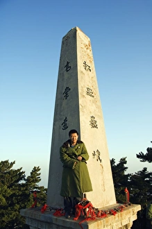 A man in green army jacket on a monument on the top of Mount Hua A man in green army jacket on a monument on the top of Mount Hua
