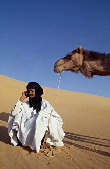 A nomad sits in the desert and talks on his mobile phone A nomad sits in the desert and talks on his mobile phone
