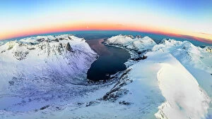Norway Collection: Panoramic aerial view of frozen fjord and majestic snowy mountains surrounding Bergsfjord at dawn