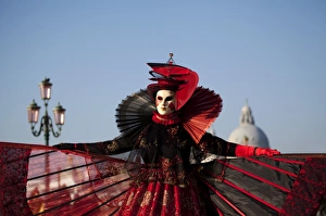 Venice, Veneto, Italy; A mask in costume on the Bacino di San Marco with the cupola of Santa Maria della Salute in Venice, Veneto, Italy; A mask in costume on the Bacino di San Marco with the cupola of Santa Maria della Salute in