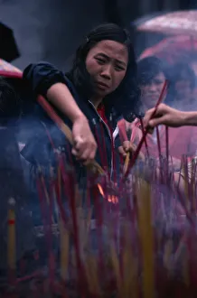 CHINA, Guangzhou Young woman lighting incense at temple CHINA, Guangzhou Young woman lighting incense at temple