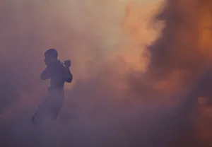 An anti-government protester runs through a cloud of tear gas holding a camera during An anti-government protester runs through a cloud of tear gas holding a camera during