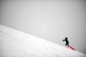 A child climbs a hill while sledging in the snow in London A child climbs a hill while sledging in the snow in London
