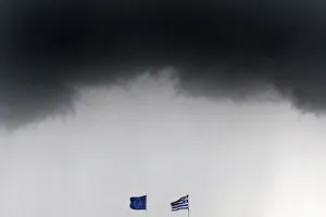 A Greek national flag and an EU flag flutter under storm clouds in Athens A Greek national flag and an EU flag flutter under storm clouds in Athens
