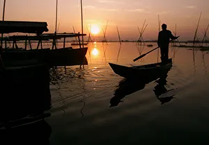 An Indonesian man rows fishing boat at sunset in central Java An Indonesian man rows fishing boat at sunset in central Java