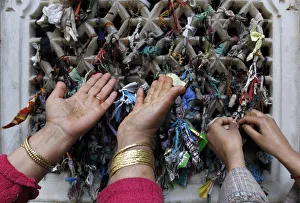 A Kashmiri Muslim woman prays as another one ties a thread on the window of the shrine of A Kashmiri Muslim woman prays as another one ties a thread on the window of the shrine of