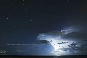 A long exposure shot shows a plane flying over the sea during a lightning storm on the A long exposure shot shows a plane flying over the sea during a lightning storm on the