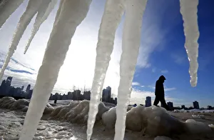 Man is framed by icicles as he walks along a beach in Chicago Man is framed by icicles as he walks along a beach in Chicago