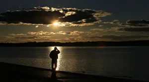 A man is silhouetted against the reflection of the sun in lake Tegel on a sunny autumn A man is silhouetted against the reflection of the sun in lake Tegel on a sunny autumn