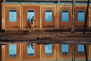 A man walking past a school is reflected in a large puddle in Niamey A man walking past a school is reflected in a large puddle in Niamey