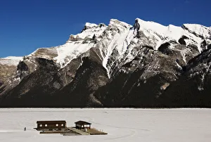 A man walks over a frozen Lake Minnewanka to a boathouse in front of the Canadian A man walks over a frozen Lake Minnewanka to a boathouse in front of the Canadian