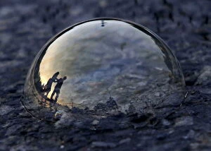Images Dated 23rd June 2015: People are reflected on a soap bubble lying on a road during the evening in New Delhi