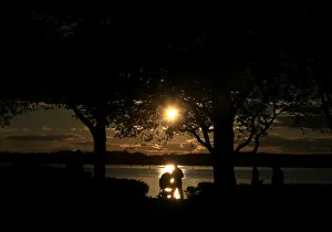 A person pushing a pram is silhouetted against the reflection of the sun in lake Tegel A person pushing a pram is silhouetted against the reflection of the sun in lake Tegel