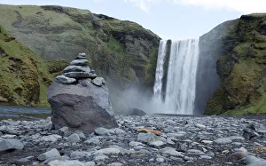 A pile of rocks stand in front of a waterfall in Skogarfoss, Iceland A pile of rocks stand in front of a waterfall in Skogarfoss, Iceland