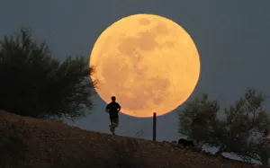 A runner makes his way along a trail on a butte in front of the super Moon at Papago A runner makes his way along a trail on a butte in front of the super Moon at Papago