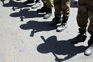 Shadows of army soldiers holding batons are cast on the ground as they stand in line to Shadows of army soldiers holding batons are cast on the ground as they stand in line to