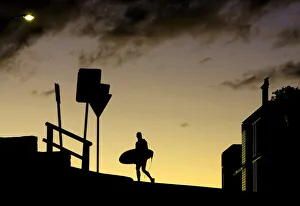 A surfer crosses the road with his board at sunset above Sydneys Bondi Beach A surfer crosses the road with his board at sunset above Sydneys Bondi Beach