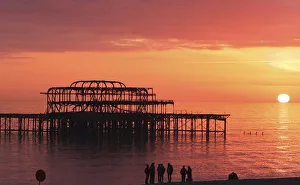 Visitors watch the sun set behind the remains of the West Pier on the seafront at Brighton Visitors watch the sun set behind the remains of the West Pier on the seafront at Brighton
