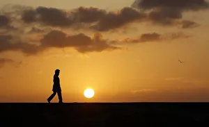 A woman walks along a breakwater at sunset in Sennen Cove, near Lands End, at the A woman walks along a breakwater at sunset in Sennen Cove, near Lands End, at the