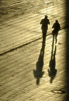 Women cast their shadows in the setting sun as they walk past the headquarters of Women cast their shadows in the setting sun as they walk past the headquarters of