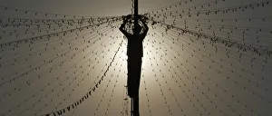 A worker is silhouetted against the setting sun while installing lights on a street A worker is silhouetted against the setting sun while installing lights on a street