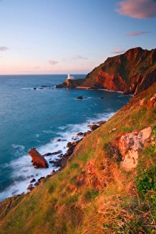 North Devon Beaches Prints: View of sea cliffs with distant lighthouse at sunset
