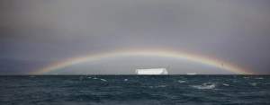 Antarctica, South Georgia, South Atlantic Ocean. A tabular iceberg floats under a low rainbow Antarctica, South Georgia, South Atlantic Ocean. A tabular iceberg floats under a low rainbow