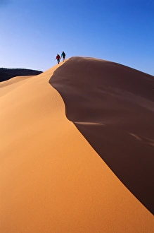 A couple walks along the crest of a golden sand dune in Coral Pink Sand Dunes State Park A couple walks along the crest of a golden sand dune in Coral Pink Sand Dunes State Park