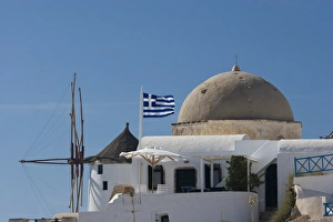 Europe, Greece, Santorini, Thira, Oia. Windmill and church dome with a Greek flag flying Europe, Greece, Santorini, Thira, Oia. Windmill and church dome with a Greek flag flying