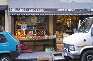 A grocery store with froits and vegetables displayed on the pavement. Cars parked in front A grocery store with froits and vegetables displayed on the pavement. Cars parked in front